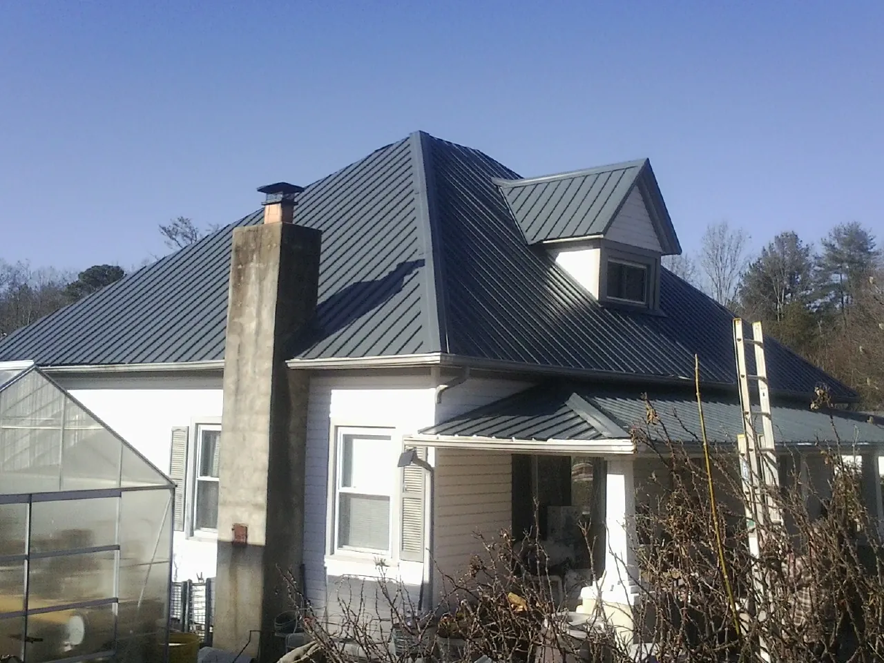 Dark blue standing seam metal roof on a white farmhouse with dormer — Slate & Tile Roof Repair by Roofing Brothers in Sciota
