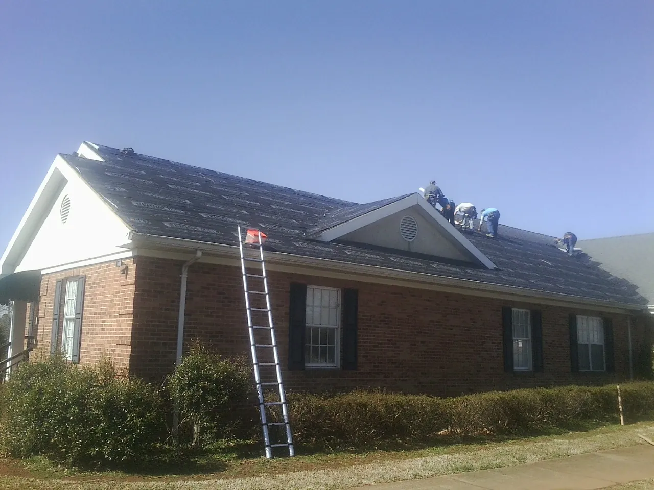 Crew tearing shingles off a brick ranch roof with a ladder set — Emergency Roof Repair work by our crew in Sciota