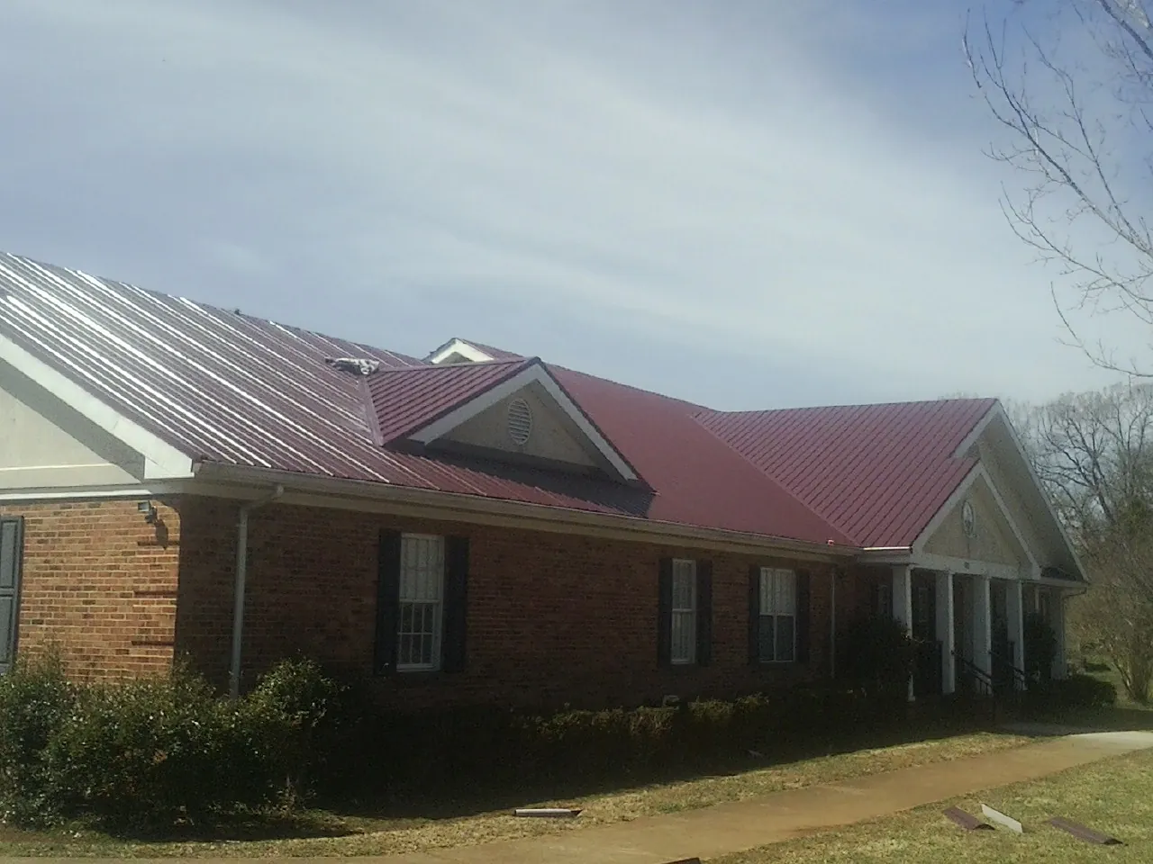 Red metal roof with gabled entries on a long brick building, from a Hail Damage Roof Repair job in Sciota