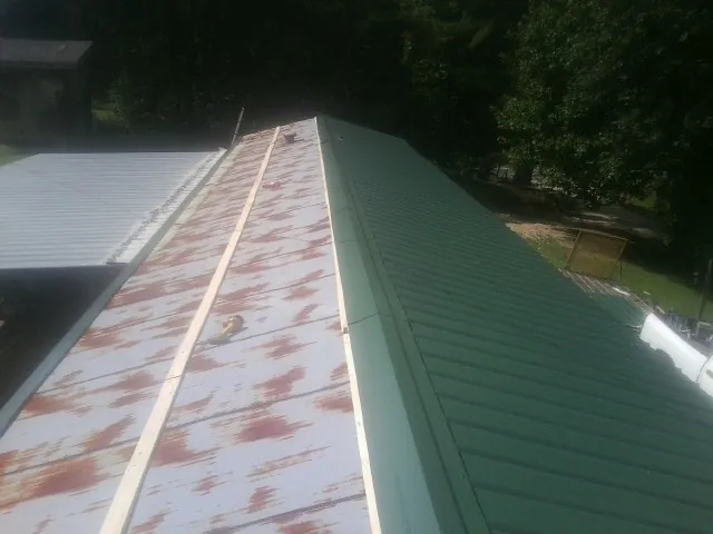 Old rusted panels beside newly installed green metal roofing — Wind Damage Roof Repair by Roofing Brothers in Sciota