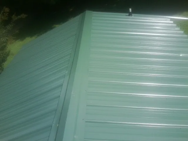 New green metal panels meeting at the ridge of a roof — Flat Roof Repair work by our crew in Sciota